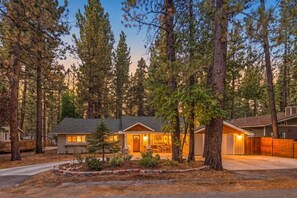 A two-story house with a front porch, surrounded by tall pine trees.