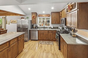 A modern kitchen with wooden cabinets, stainless steel appliances, and a large window. - Outdoor Living by Snow Summit! Big Bear Mural! PET FRIENDLY! HOT TUB! Fire Pit! Large Fenced Yard! (Big Bear Lake)