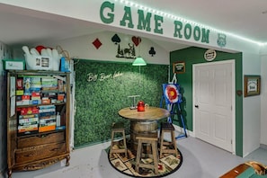 A game room with a bookshelf, a round table, and a green wall. - Outdoor Living by Snow Summit! Big Bear Mural! PET FRIENDLY! HOT TUB! Fire Pit! Large Fenced Yard! (Big Bear Lake)