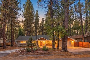 A two-story house with a covered porch, surrounded by tall pine trees. - Outdoor Living by Snow Summit! Big Bear Mural! PET FRIENDLY! HOT TUB! Fire Pit! Large Fenced Yard! (Big Bear Lake)