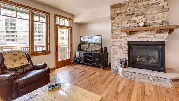 A living room with a stone fireplace, a leather sofa, a television, and large windows. - Beautiful 1 bedroom, 1 bath condo on Lake Dillon in Frisco. Walk to shuttle. (Frisco)