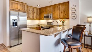 A kitchen with wooden cabinets, stainless steel appliances, granite countertops, and a bar stool. - Beautiful 1 bedroom, 1 bath condo on Lake Dillon in Frisco. Walk to shuttle. (Frisco)