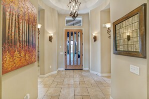 Stunning hallway with a wooden door, glass panels, and a beautiful chandelier.