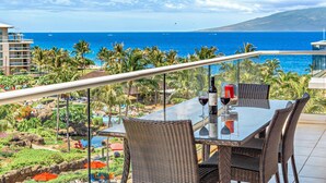Un balcon avec une table en verre et des chaises en osier, offrant une vue sur la piscine et l’océan.