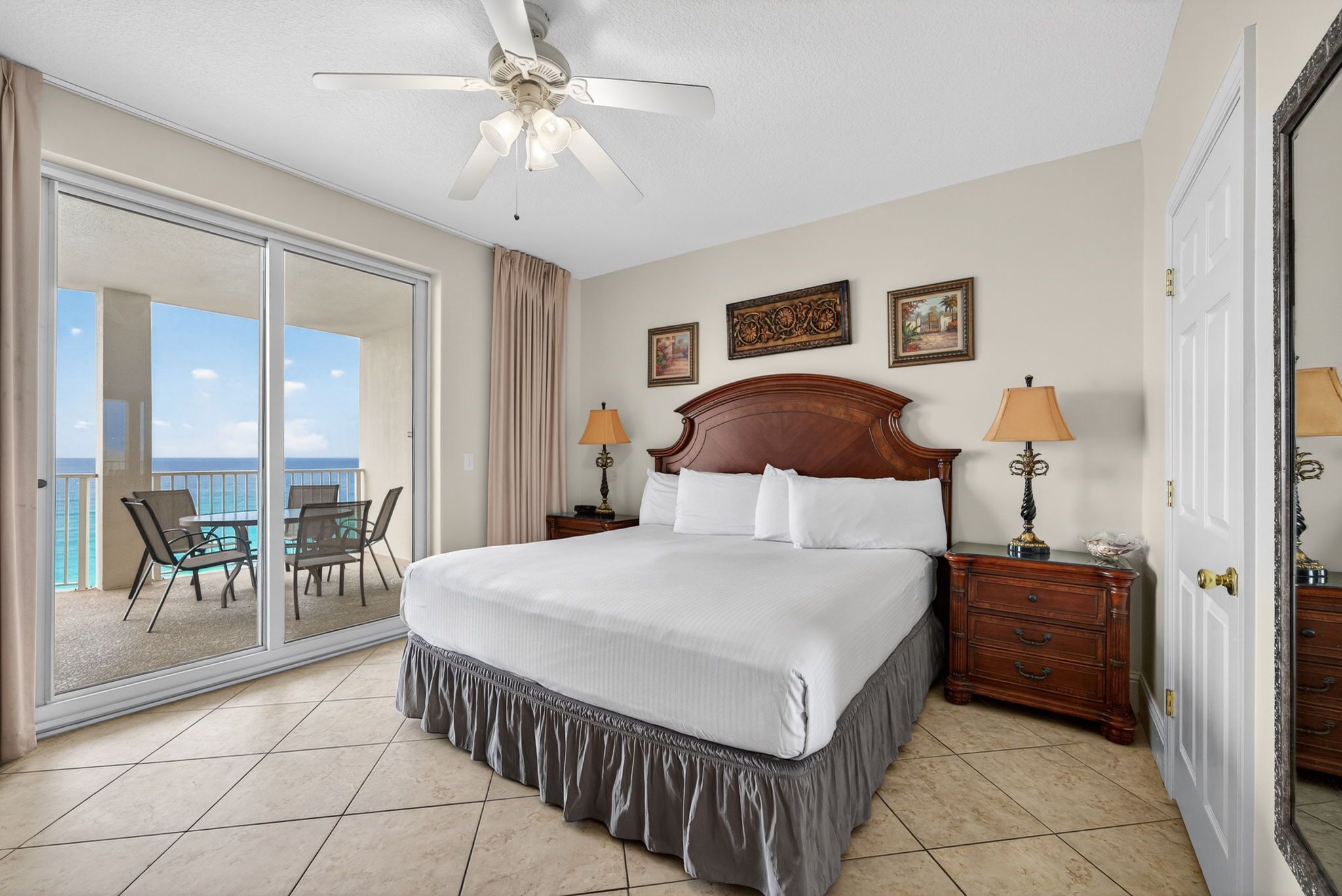 A hotel room with a large bed, two bedside tables, a ceiling fan, and a balcony with a view.