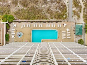 Un hotel moderno con piscina en la azotea, varios balcones y una zona de playa con tumbonas.