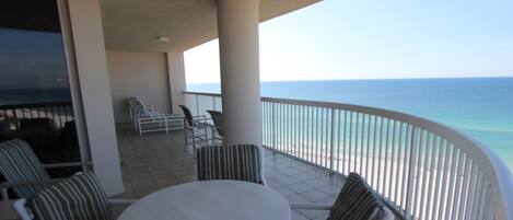 A balcony with a white table and striped chairs, overlooking a beach.