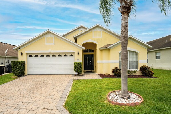 A two-story house with a garage, a front yard with a palm tree, and a well-maintained lawn. - Spacious Pool Home with Spa in Quiet Community Close to Disney (Davenport)