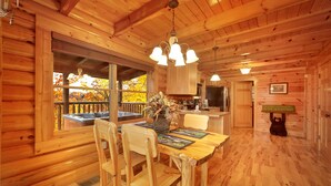 L’intérieur d’un chalet en bois comprend une table à manger, des chaises, un lustre, un coin cuisine et une décoration sur le thème de l’ours.