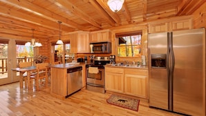 Une cuisine rustique, située dans une cabane en bois, avec un îlot central, des appareils en acier inoxydable et un grand réfrigérateur.