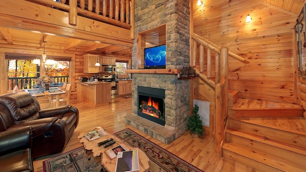 Un intérieur spacieux de chalet en bois, avec une cheminée en pierre, un canapé en cuir, un coin repas et une cuisine.