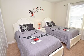 Ein Schlafzimmer mit zwei Betten, jedes mit einer Bettdecke und Kissen im Mickey Mouse Design.
