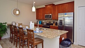 A modern kitchen with granite countertops, wooden cabinets, stainless steel appliances, and a dining area with wooden chairs. - Stunning Town Home with Splash Pool in Champions Gate Resort - Close to Theme Parks (Davenport)