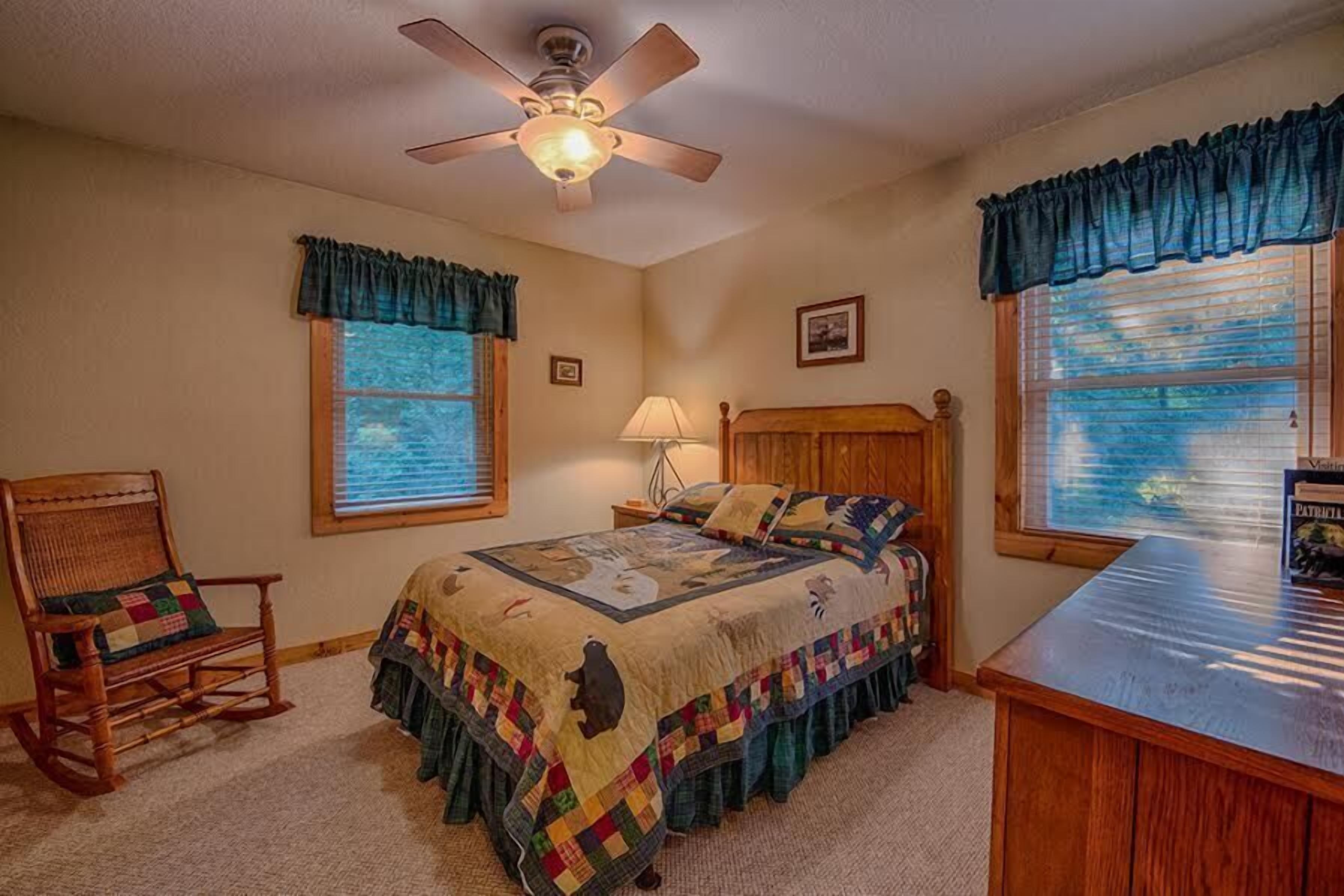 A bedroom with a bed, a rocking chair, a desk, and a ceiling fan.