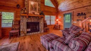 Ein gemütliches Blockhaus-Interieur mit Kamin aus Stein, Holzwänden, einer Couch und einem Esstisch.