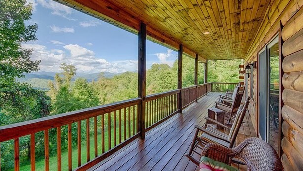 Eine Holzterrasse mit Geländer, mit Stühlen und einem Tisch möbliert, mit Blick auf eine Berglandschaft.