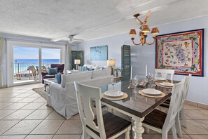 A dining area with a table set for four, white chairs, and a view of the ocean through large sliding doors. - 🌊 Islander #607 – Panoramic Gulf Views & Total Beachfront Luxury! 🏖️✨ (Destin)