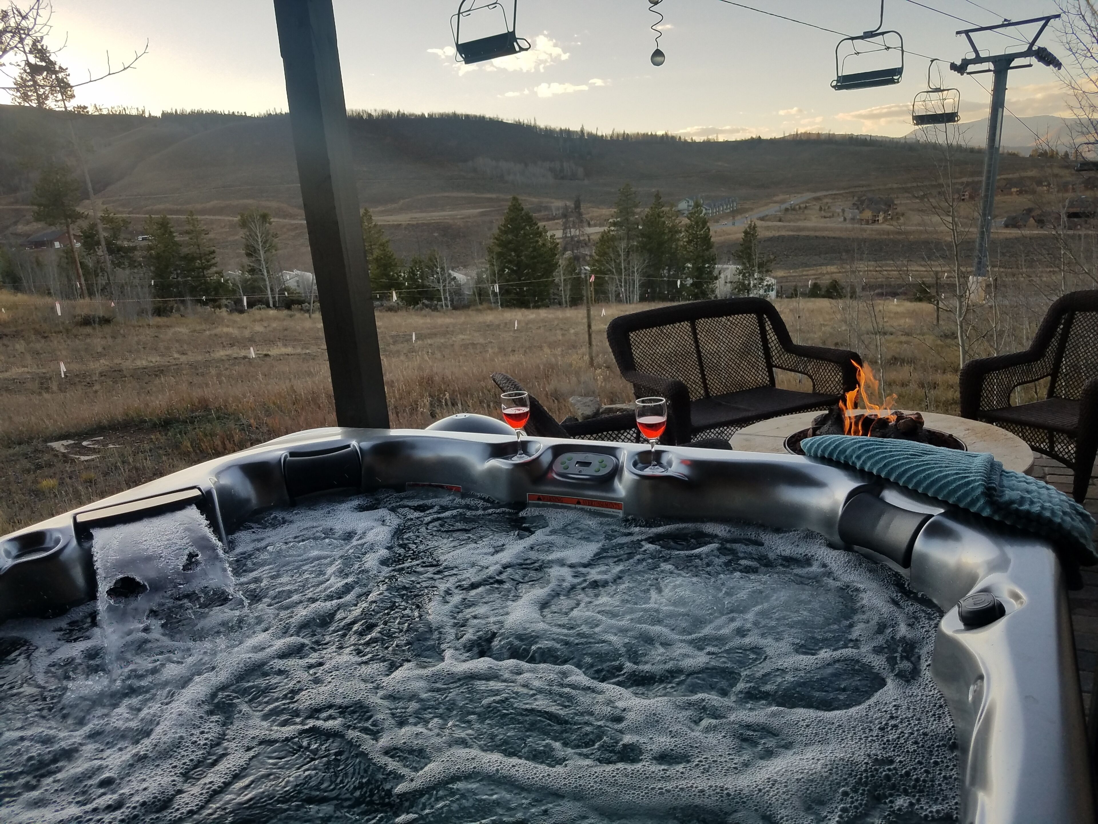 Ein Whirlpool mit Blick auf eine gebirgige Landschaft, zwei Stühle und ein Glas Rotwein.