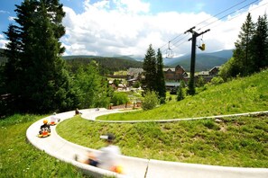 Une route sinueuse offrant une vue sur la montagne, un télésiège et, au loin, un bâtiment doté d’un toit en pente.