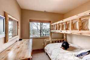 Une chambre avec des lits superposés, un bureau en bois et une fenêtre donnant sur les arbres.