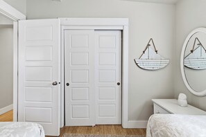 A bedroom with a white door, a bedside table, a bed with a white bedspread, and two wall decorations. - Dune Grass Cottage-Charming, steps to beach (Cloverdale)