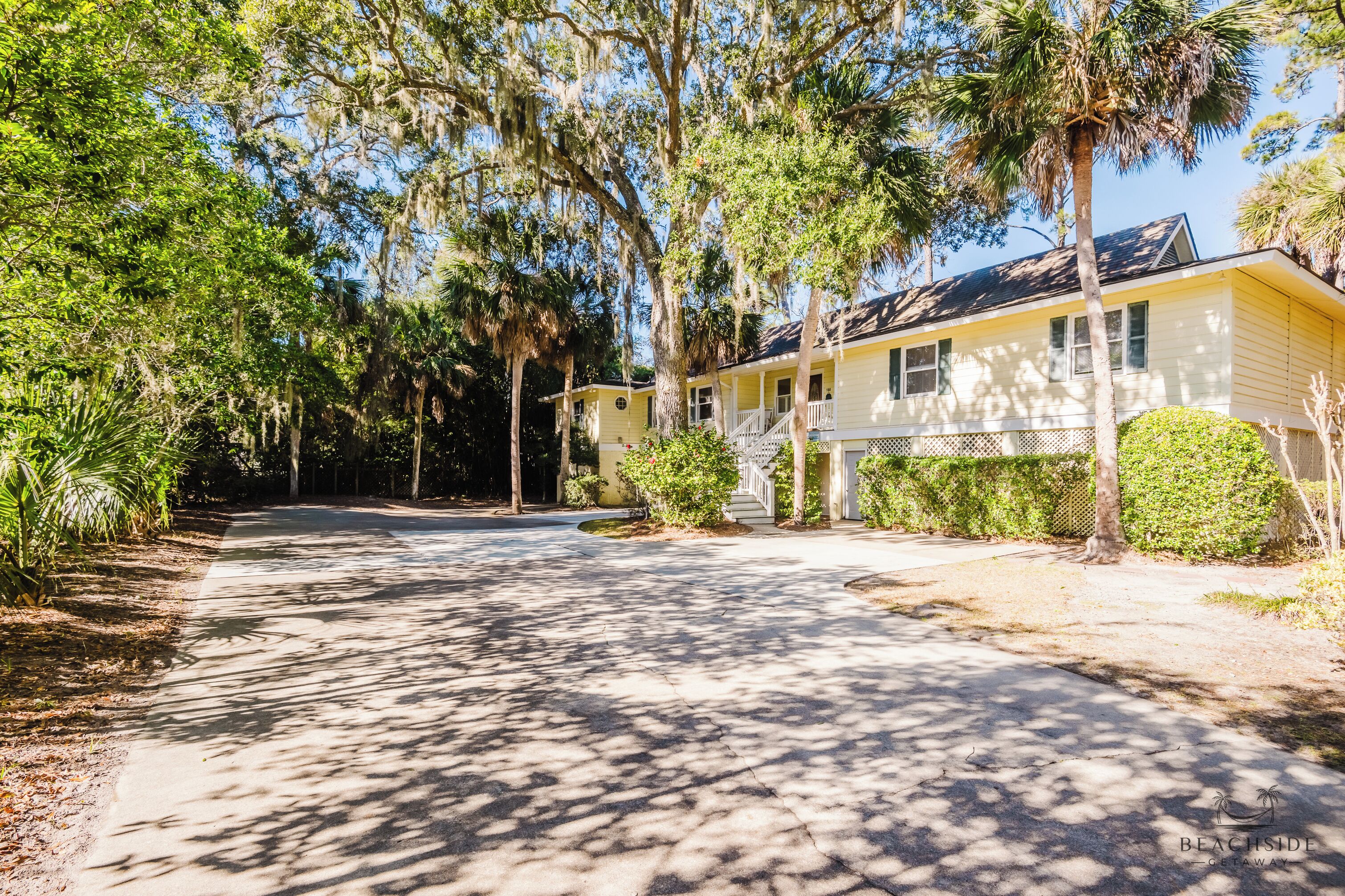 A yellow building with a porch and a covered driveway, surrounded by trees and greenery.