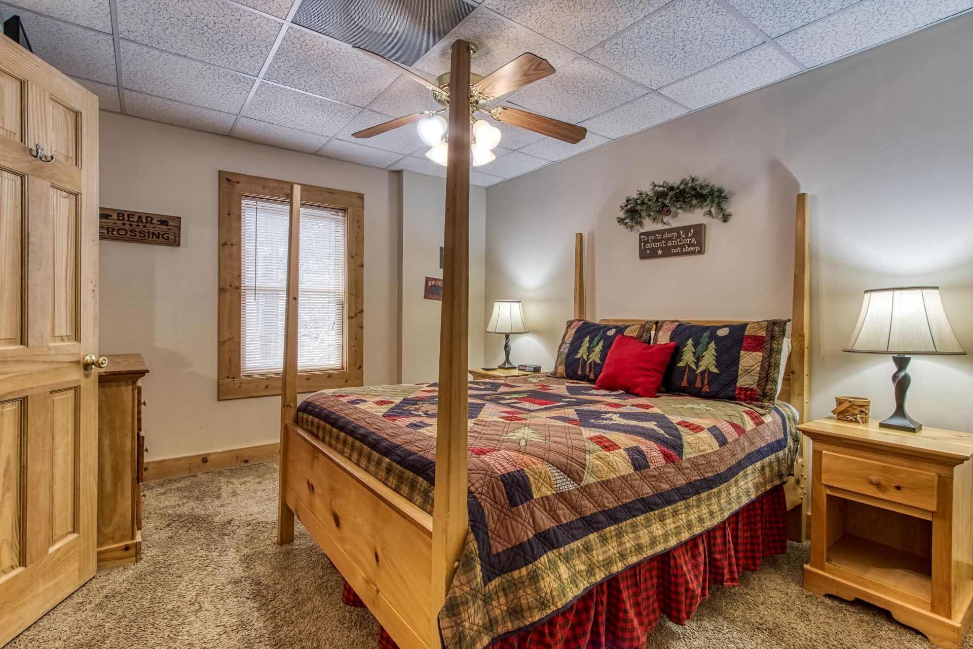 A bedroom with a four-poster bed, two bedside tables, a ceiling fan, and a window with blinds.