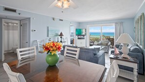 A spacious living area with a dining table, chairs, a sofa, and a balcony with a view of the sea.