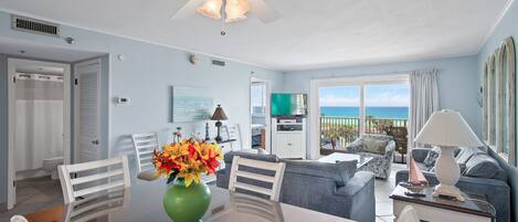 A spacious living area with a dining table, chairs, a sofa, and a balcony with a view of the sea.