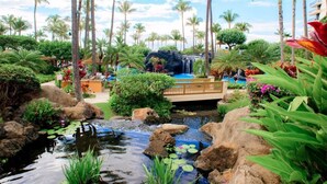 Um resort tropical com uma cascata, palmeiras e um pequeno lago com nenúfares.