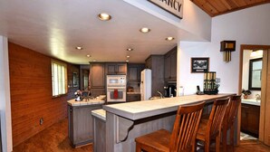 A kitchen with wooden cabinets, a central island with bar stools, built-in appliances, and recessed ceiling lighting. - Falling Leaf Retreat by Destination Big Bear : Lake Views! Hot Tub! Private! Fireplaces! Internet! Pool Table! (Big Bear Lake)