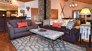 A cozy living room with a sofa, a coffee table, and a fireplace. A sign indicating 'VACANCY' is visible in the background. - Falling Leaf Retreat by Destination Big Bear : Lake Views! Hot Tub! Private! Fireplaces! Internet! Pool Table! (Big Bear Lake)