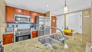 A kitchen with granite countertops, stainless steel appliances, wooden cabinets, and a hanging light fixture.