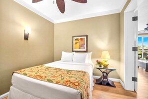 A hotel room with a bed, a nightstand with a lamp, a framed picture on the wall, and a view of the outside. - Honua Kai | Ocean View 2 BR | Family friendly | Car Incl. w/ 6+ Nights | HKH-242 by KBM (Lahaina)