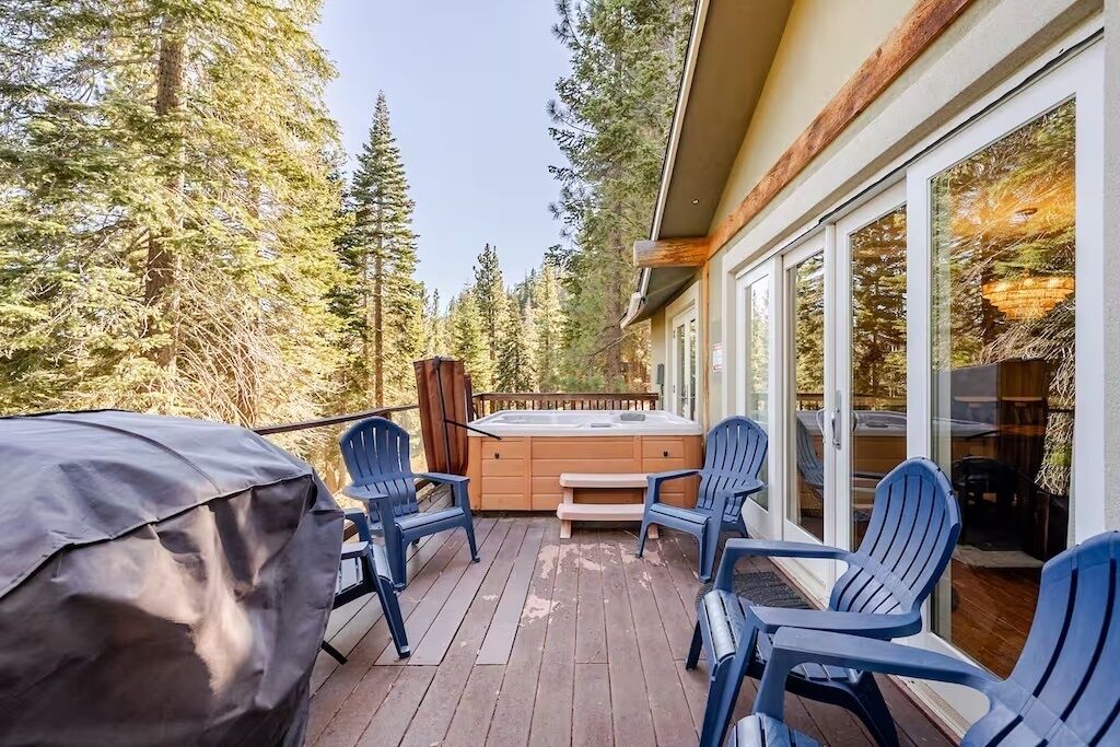 A deck with Adirondack chairs and a hot tub, surrounded by a forest.