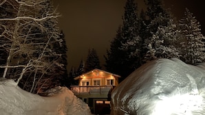 Lumipeitteinen maisema, jossa on parvekkeellinen talo ja sen ympärillä puita.