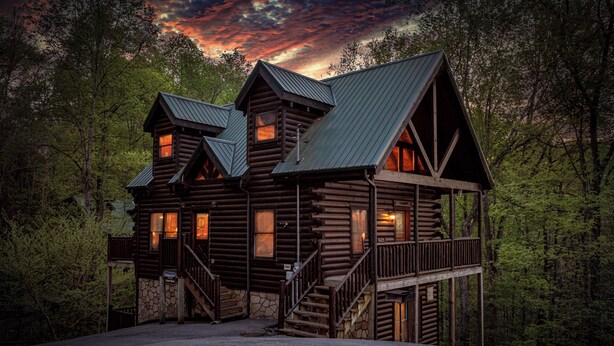 A log cabin with multiple windows, a stone foundation, and a wooden deck. - Private Indoor Pool Cabin • 2 King Suites (Sevierville)