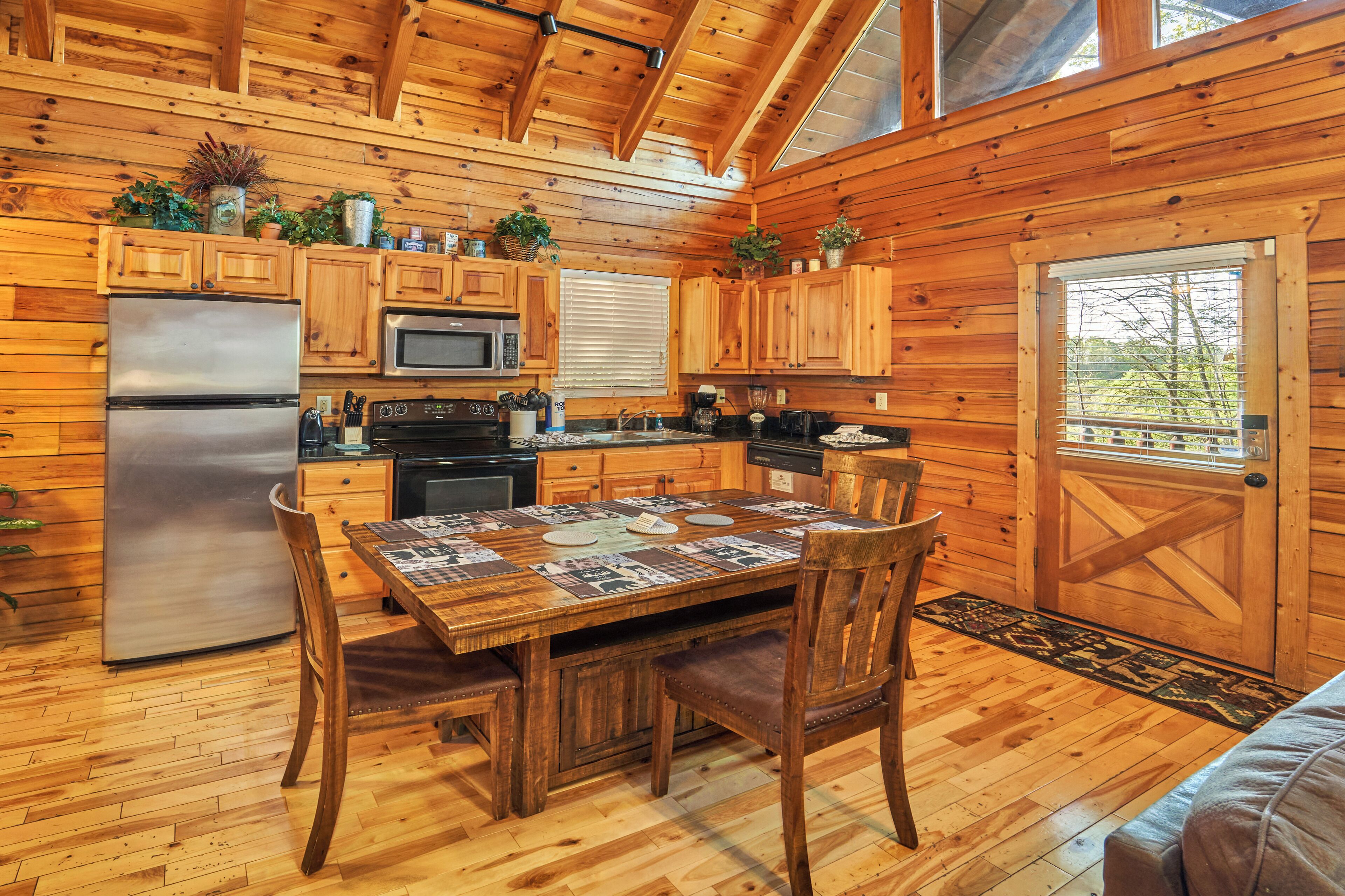 A wooden cabin kitchen with a dining table, chairs, a refrigerator, stove, microwave, and cabinets.