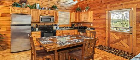 A wooden cabin kitchen with a dining table, chairs, a refrigerator, stove, microwave, and cabinets.