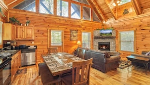 A spacious cabin with a wooden interior, a dining area, a fireplace, and a television mounted on the wall. - Private Indoor Pool Cabin • 2 King Suites (Sevierville)