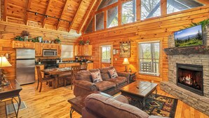 A cozy cabin interior with a wooden interior, a stone fireplace, a kitchen area, and a seating area with a couch and coffee table. - Private Indoor Pool Cabin • 2 King Suites (Sevierville)