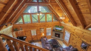 A spacious log cabin with a loft bedroom, a fireplace, and large windows offering a view of the surrounding forest. - Private Indoor Pool Cabin • 2 King Suites (Sevierville)
