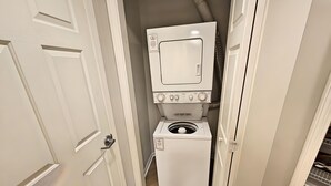 A compact laundry room with a front-loading washer and dryer, white cabinetry, and a wooden floor.