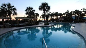 A swimming pool with a clear view of the water, surrounded by palm trees and lounge chairs.