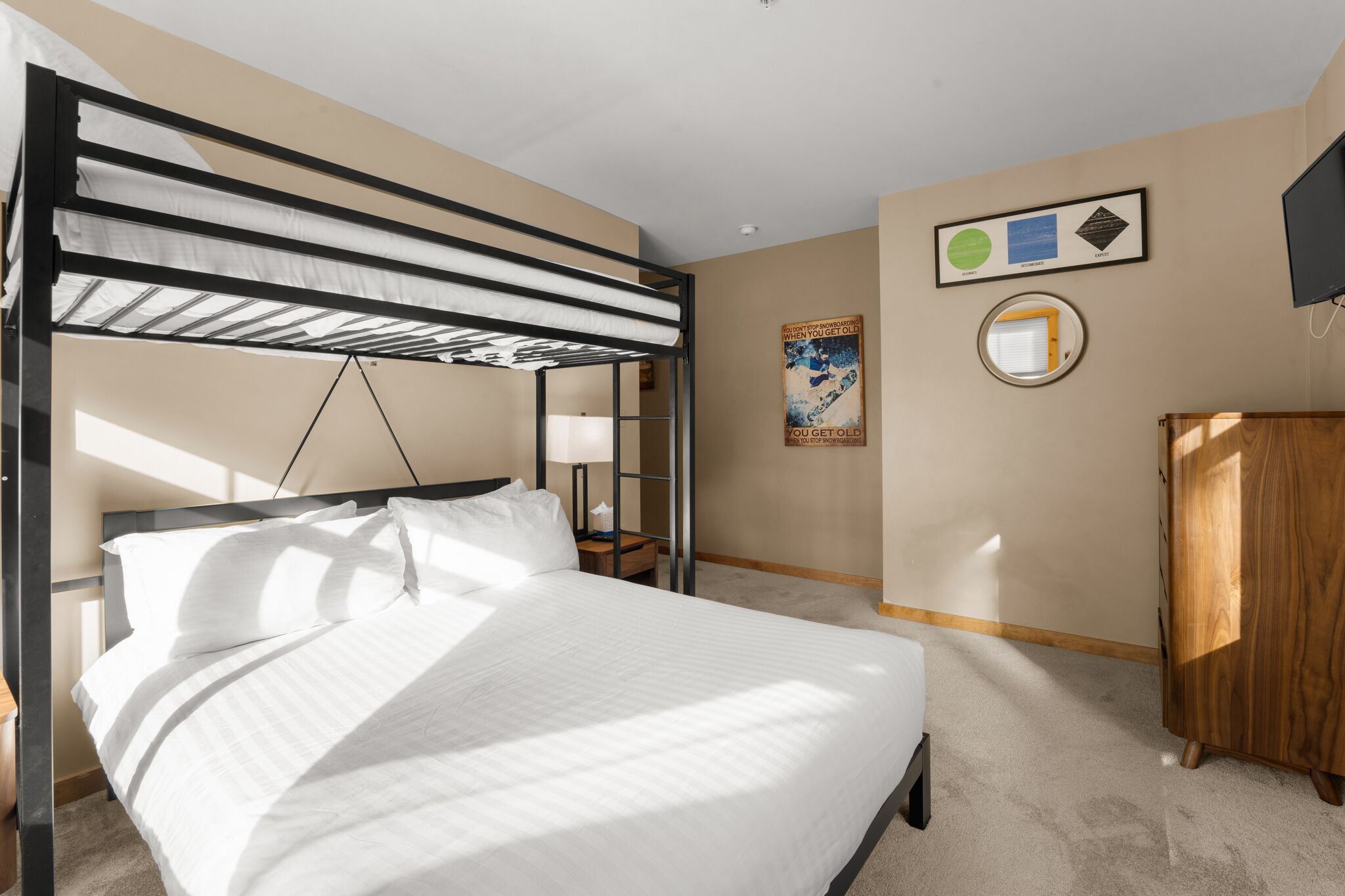 Un lit superposé avec une table de chevet et une lampe, une armoire en bois et un tableau encadré au mur.