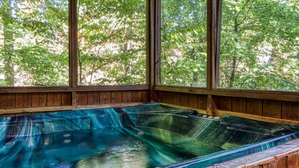 Ein Whirlpool mit Holzvertäfelung und großen Fenstern mit Blick auf einen bewaldeten Bereich.