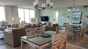 Een ruime woonkamer met een eethoek, grote ramen en een moderne kroonluchter.