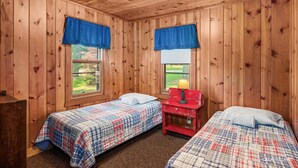 A room with wooden paneled walls, two beds with plaid bedding, a red nightstand, and a window with a view of greenery. - Lakefront Cabin #5 The Bass (Presque Isle)