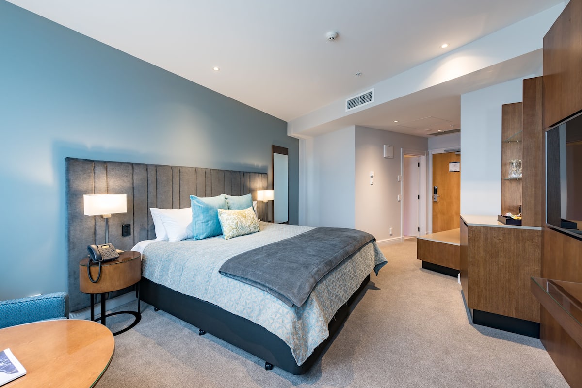 Een moderne hotelkamer met een groot bed, nachtkastje, lamp en een televisie.