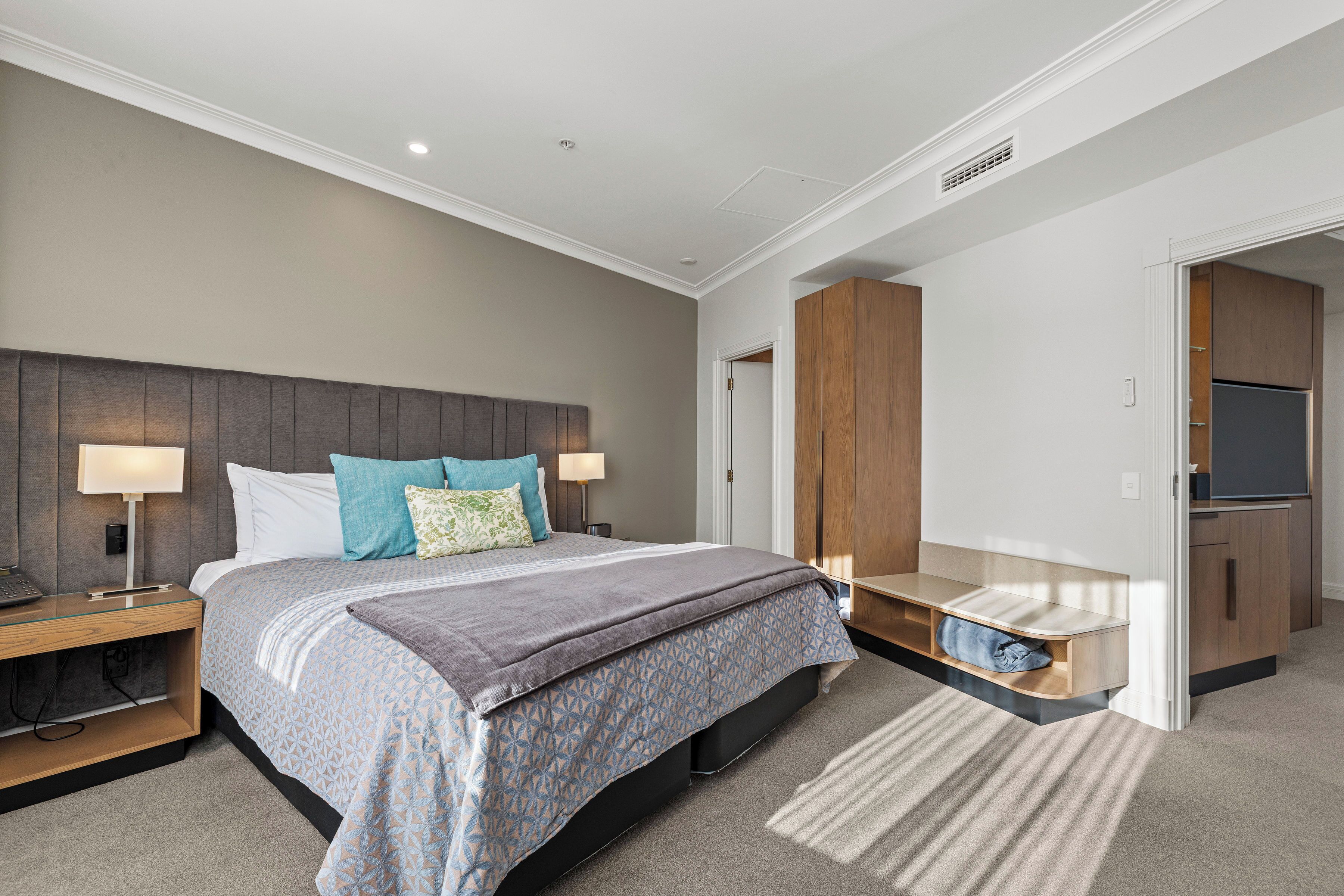 Een moderne slaapkamer met een bed, nachtkastjes, een ingebouwde bank, een garderobe en een televisie.